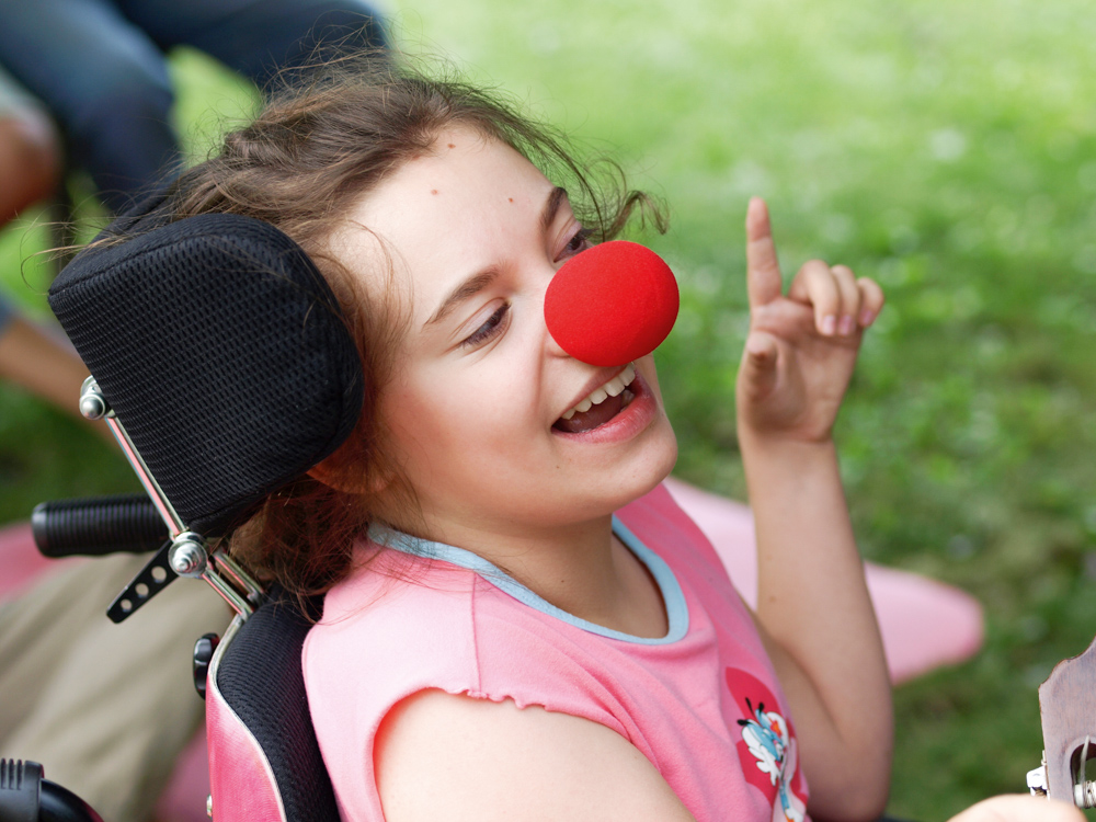 Mädchen im Rollstuhl mit roter Schaumstoffnase lacht