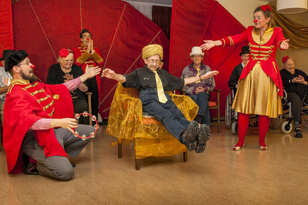 Zwei Clowns präsentieren den Auftritt eines Seniors, der auf einem Nagelbrett in einem Stuhl balanciert