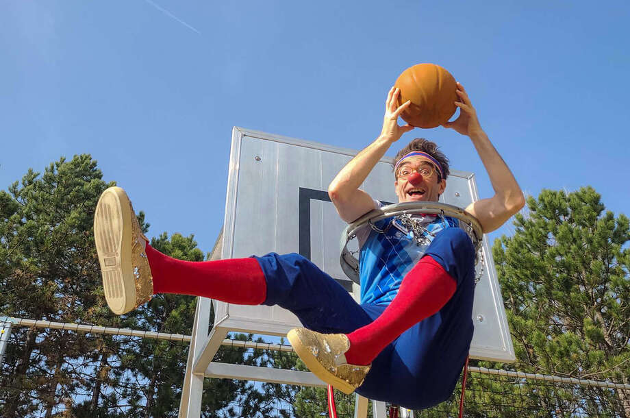 Clown Bernhart sitzt in einem Basketballkorb und hält einen Ball.