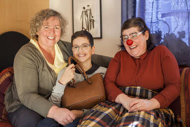 Mutter, Kind und Clownin sitzen auf einer Couch und lachen