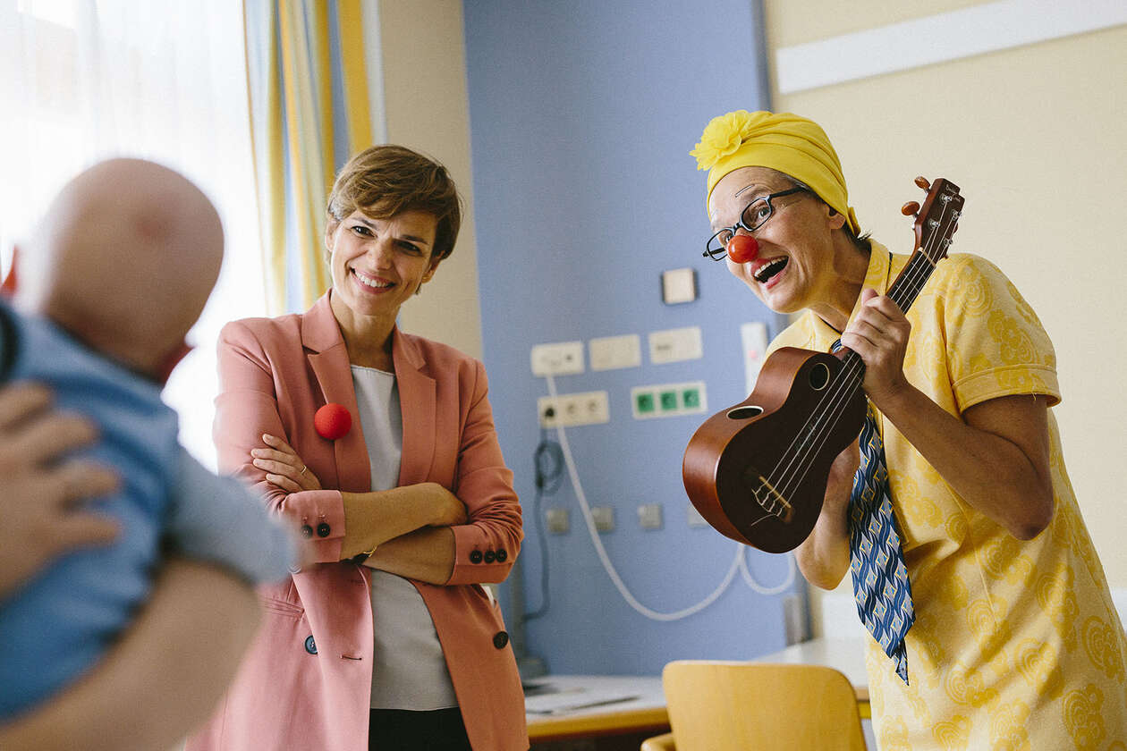 Clownin mit Ukulele und Gesundheitsministerin Rendi-Wagner interagieren mit einem Baby