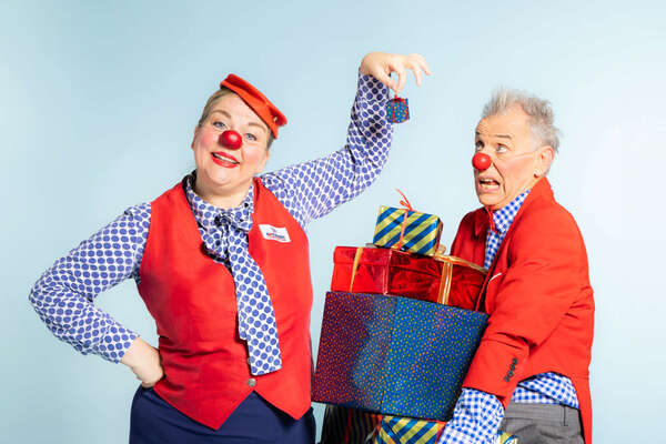 Zwei ROTE NASEN Clowns mit einem Stapel Geschenken in der Hand.
