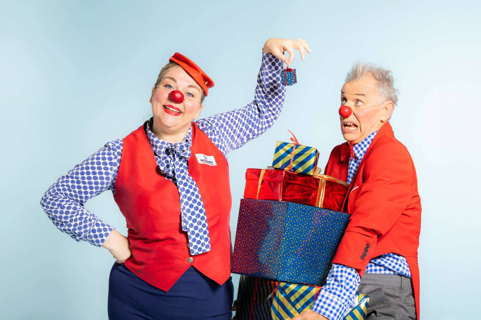 Zwei ROTE NASEN Clowns mit einem Stapel Geschenken in der Hand.