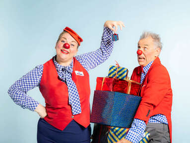 Zwei ROTE NASEN Clowns mit einem Stapel Geschenken in der Hand.
