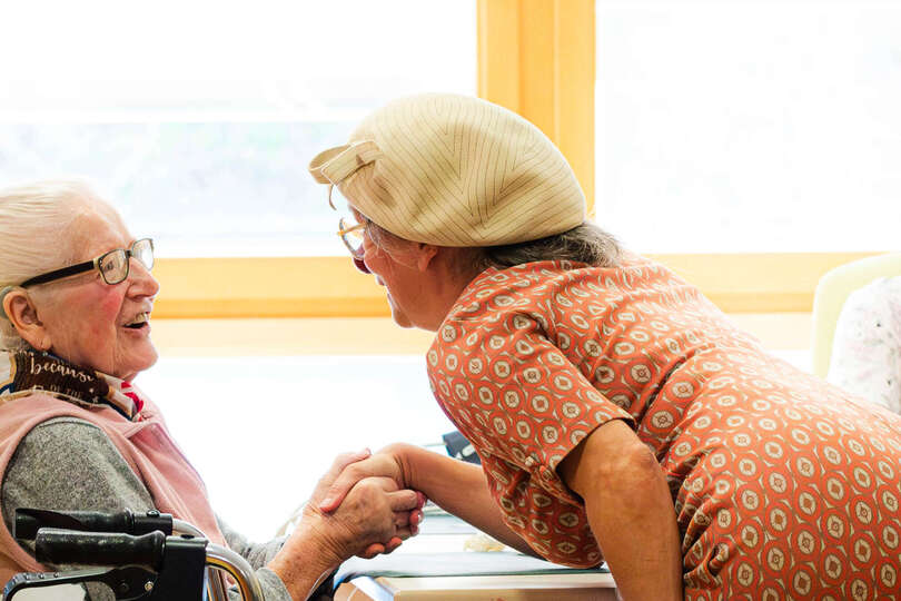 Clownin Herta gibt einer Bewohnerin im Pflegeheim die Hand.