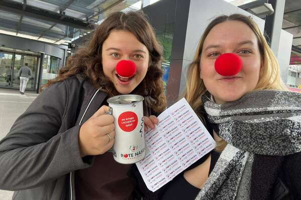 Zwei Schülerinnen mit roter Nasen und Spendendose beim Spendensammeln.