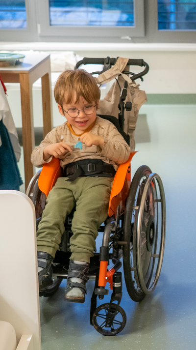 Junge im Rollstuhl mit einer kleinen blauen Feder in der Hand