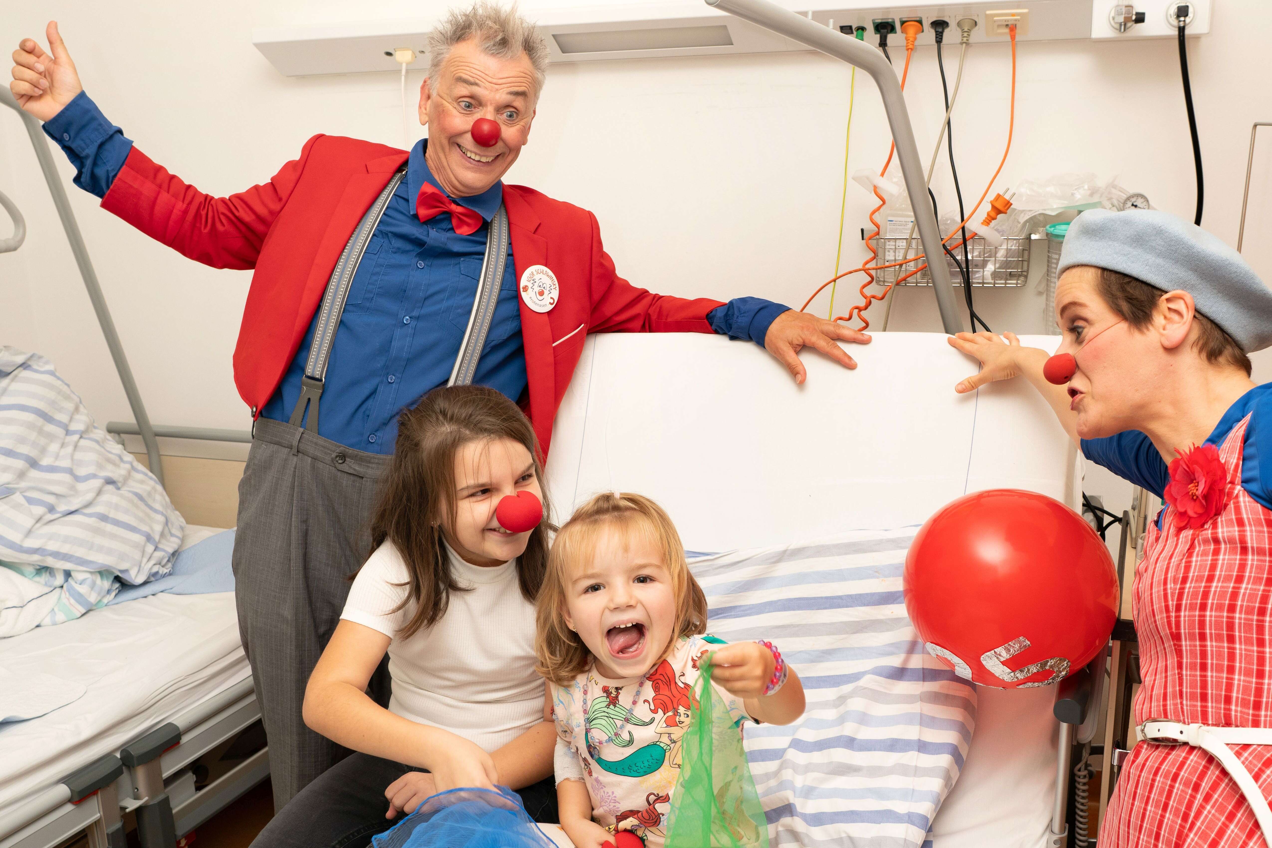 Zwei ROTE NASEN Clowns bringen Kinder im Krankenhausbett zum Lachen.
