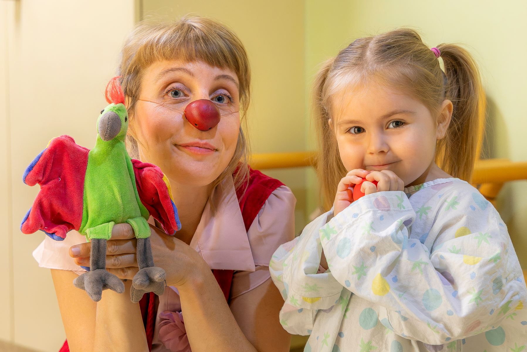 Ein kleines Mädchen mit einer roten Nase in der Hand neben Clownin Lilo und ihrer Handpuppe.