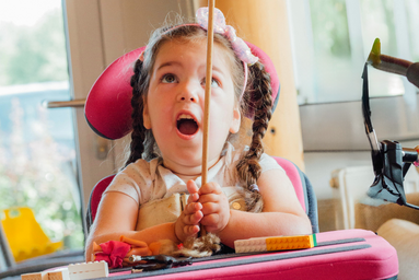 Ein Mädchen im Rollstuhl balanciert einen Teller auf einem Stäbchen.