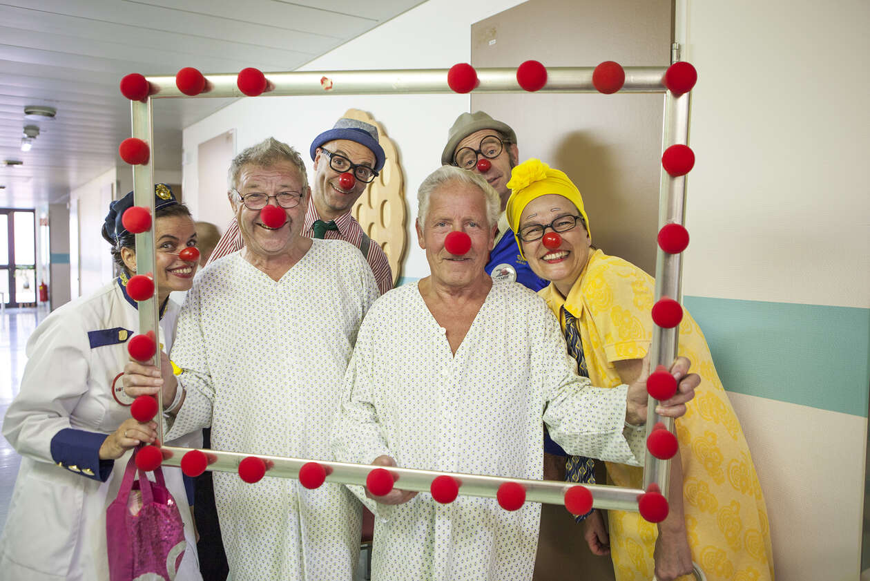 Gruppe von Clowns und zwei ältere männliche Patienten posieren mit einem überdimensionalen Bilderrahmen mit roten Schaumstoffnasen