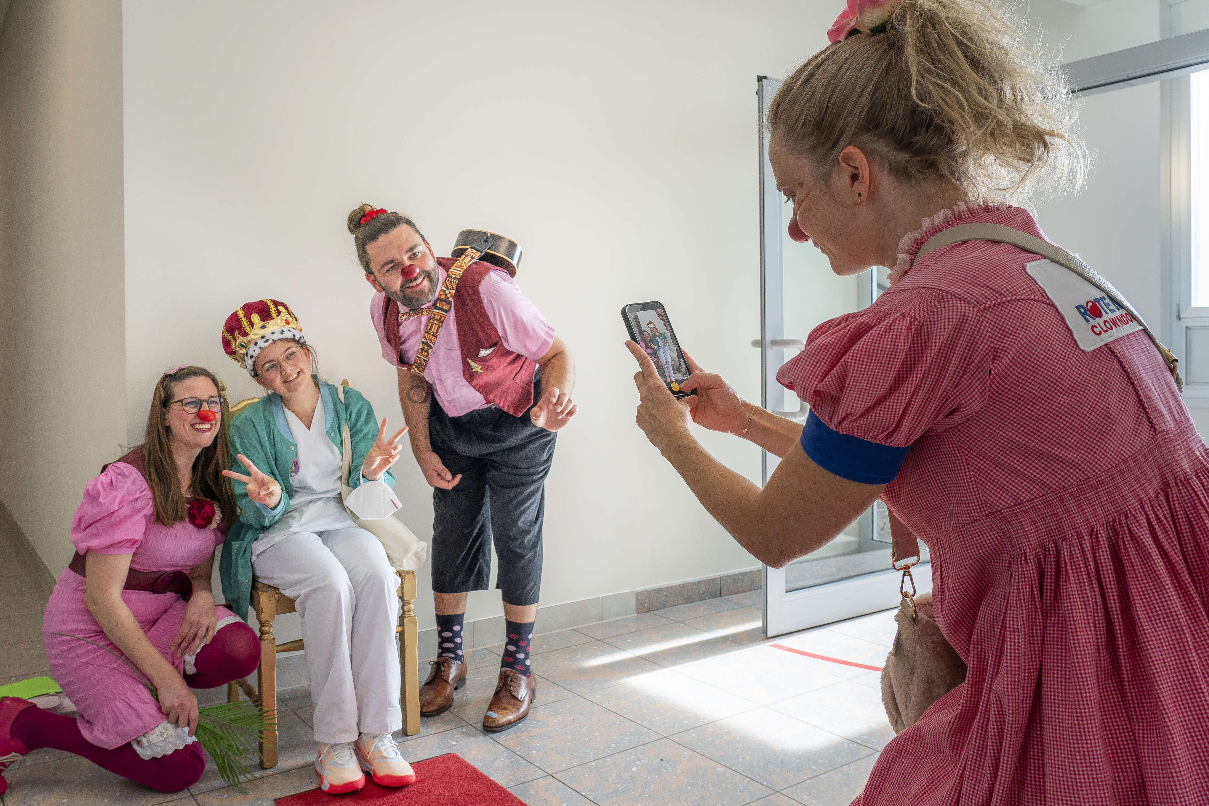 Eine ROTE NASEN Clownin fotografiert zwei Clowns und eine verkleidete Pflegekraft, die lachend für ein Bild posieren.