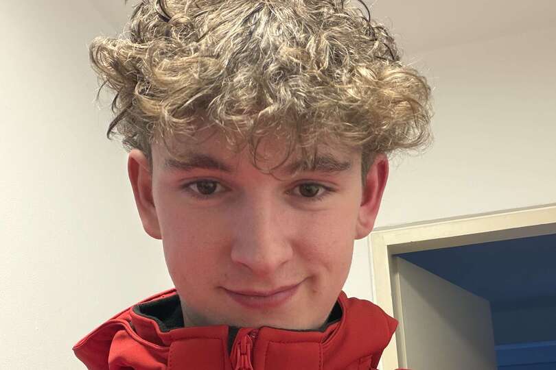 Eine junge Person mit lockigen Haaren und roter Jacke lächelt.