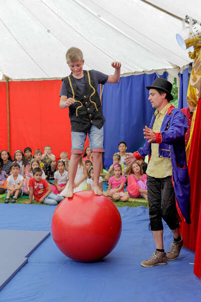 Ein Junge balanciert auf einem großen roten Ball und bewegt sich damit vorwärts