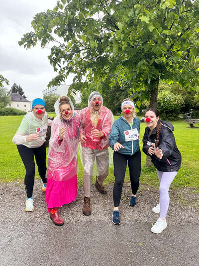Gruppenbild mit drei hochmotivierten Teilnehmer*innen und zwei ROTE NASEN Clowns, die trotz Regen Spaß beim ROTE NASEN LAUF hatten.