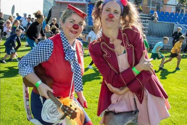 ROTE NASEN-Clownin Ecki mit Gitarre und Kollegin vor einer Tribüne während eines ROTE NASEN-Laufs.