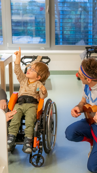 Junge im Rollstuhl zeigt lächelnd in die Luft.