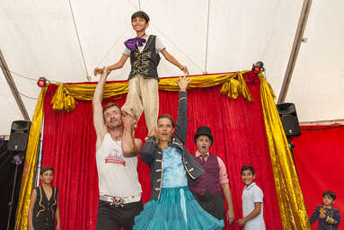 Zwei Clowns zeigen ein Kunststück mit einem Bub, der auf ihren Schultern steht.