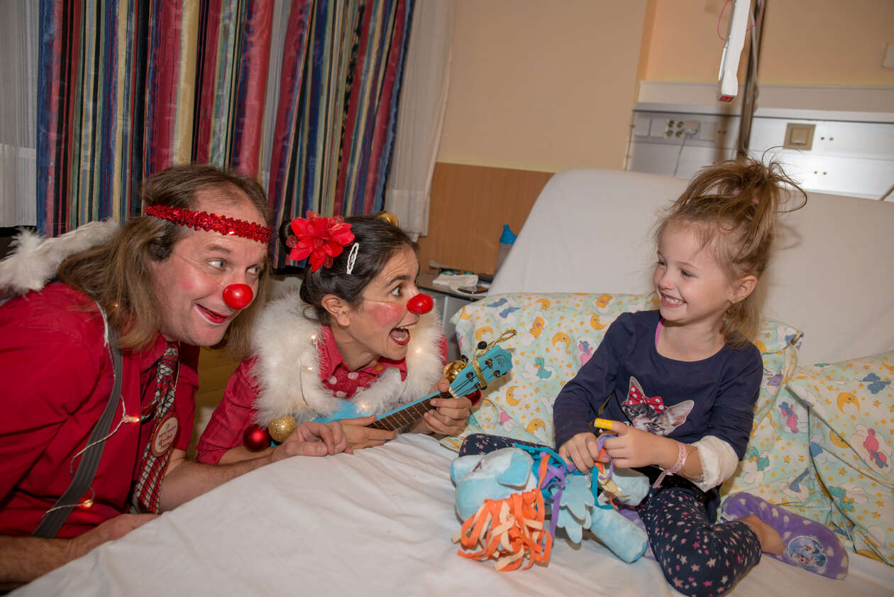 Clown und Clownin singen und musizieren für kleines lachendes Mädchen im SPitalsbett