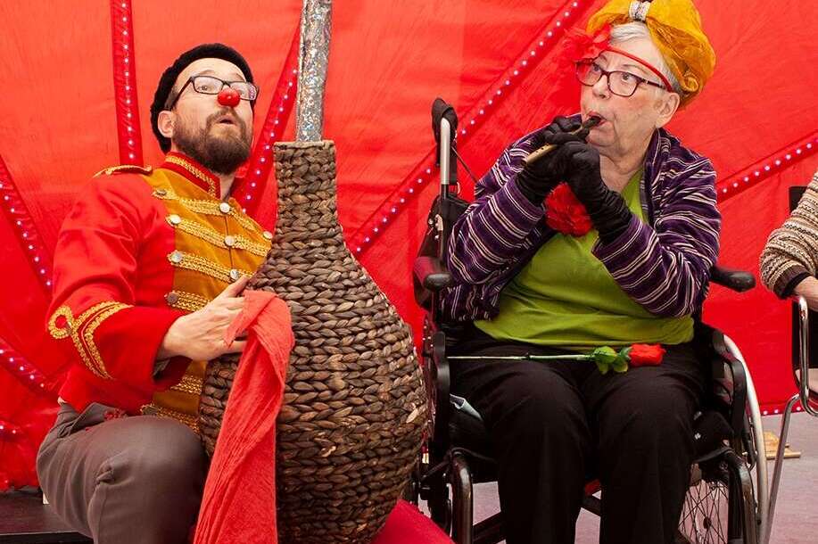 Seniorin spiel Flöte, Clown sitzt neben Korb mit Schlange