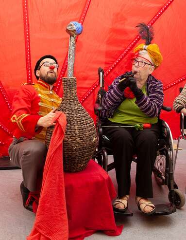 Seniorin spiel Flöte, Clown sitzt neben Korb mit Schlange 