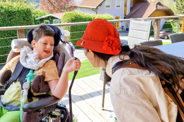ROTE NASEN-Clownin Carmensita und ein Jugendlicher im Rollstuhl auf einem Balkon.