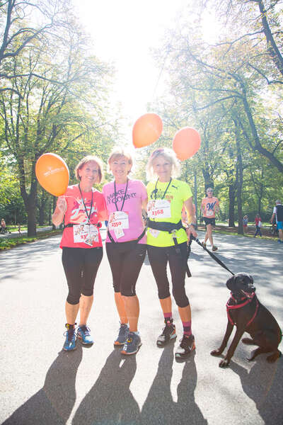 Drei Läuferinnen posieren mit ihrem Hund und Luftballoons