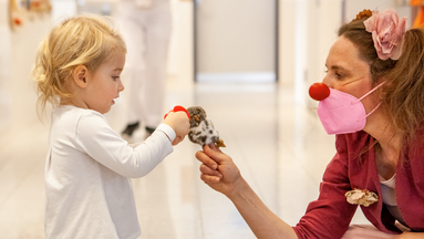 Ein kleines Mädchen und ROTE NASEN-Clownin Traudi, die einen kleinen Vogel in den Händen hält.