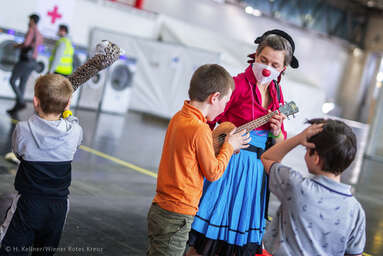 ROTE NASEN-Clownin Irmi mit Ukulele vor Kindern anlässlich des Weltflüchtlingstags 2022 in der Messe Wien.