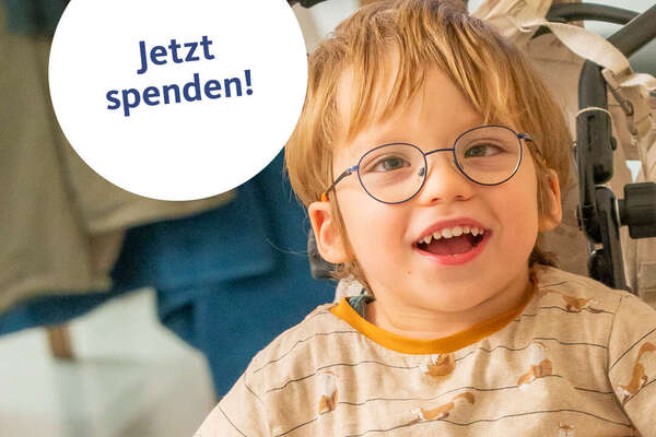 Junge im Rollstuhl lächelt in die Kamera. Weißer Kreis mit "Jetzt spenden" Aufschrift.