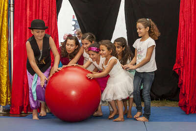 Kinder rollen gemeinsam einen großen roten Ball