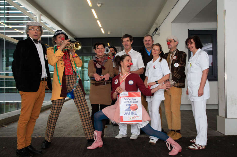 Gruppe von Clowns und Pflegepersonal des LKH Leoben posieren für ein Foto, eine Clownin hält ein kleines Plakat mit der Aufschrift 20 Jahre Jubiläum Leoben in der Hand