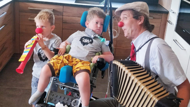 ROTE NASEN-Clown Guido spielt vor zwei Kindern Ziehharmonika.