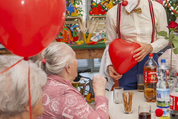 ROTE NASEN-Clown Bernhart mit einem großen, roten Herz in der Hand bei einem Besuch älterer Damen.