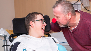 Ein Jugendlicher im Rollstuhl und ein Erwachsener, der eine rote Schaumstoffnase trägt.