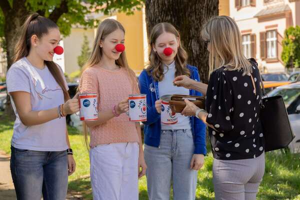 Drei junge Schülerinnen bei der ROTE NASEN Straßensammlung mit Spendendosen in der Hand und einer Spenderin.