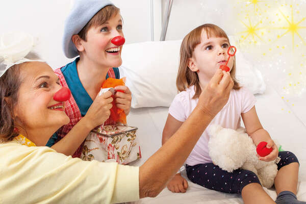 ROTE NASEN-Clowninnen Aurelia, Betti und ein Mädchen beim gemeinsamen Seitenblasen.