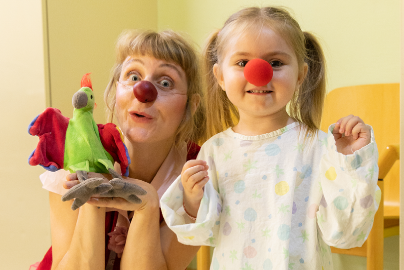 Ein kleines Mädchen mit einer roten Nase neben Clownin Lilo und ihrer Handpuppe.