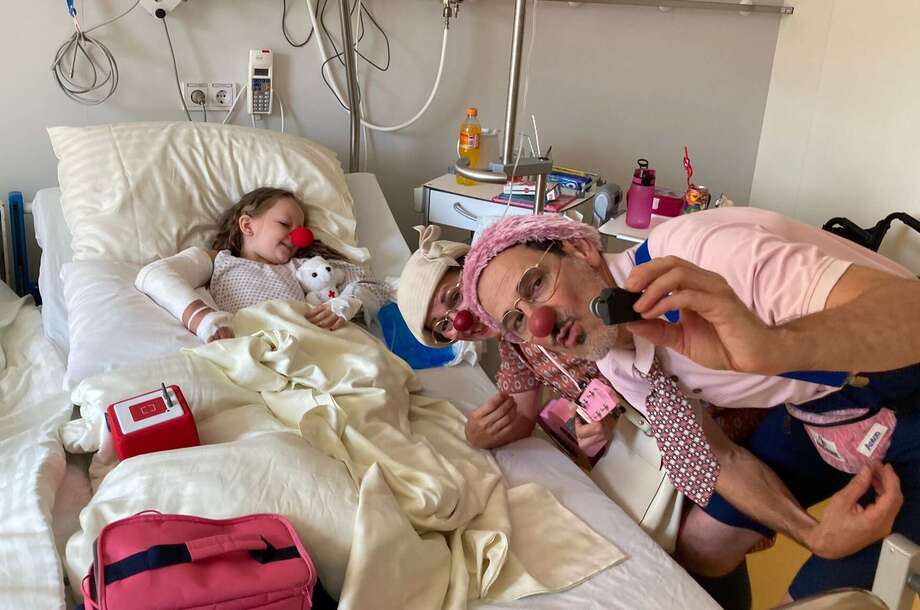 Das Mädchen Frida liegt im Krankenbett und macht Fotos mit zwei ROTE NASEN Clowns.