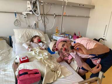 Das Mädchen Frida liegt im Krankenbett und macht Fotos mit zwei ROTE NASEN Clowns.