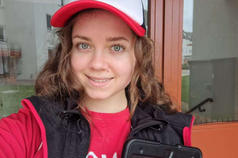 Eine junge Werberin lächelt in die Kamera. Sie trägt eine rote Jack und hat ein Tablet bei sich.