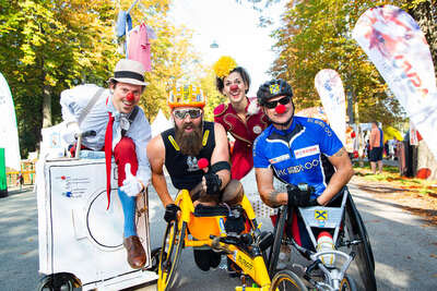Thomas Geierspichler und Kollege im Rennrollstuhl posieren gemeinsam mit zwei ROTE NASEN Clowns auf der Laufstrecke des ROTE NASEN LAUFS
