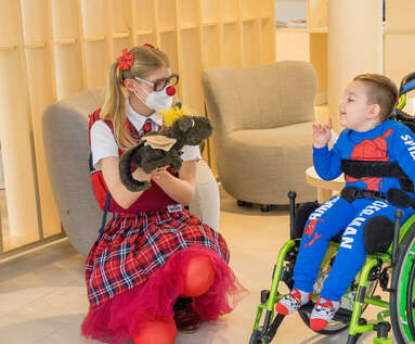 ROTE NASEN-Clownin Josefine mit Stofftier in der Hand und ein kleiner Junge in seinem Rollstuhl.