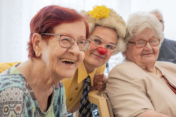 Clownin Zitronella lacht mit zwei Seniorinnen im Pflegeheim.