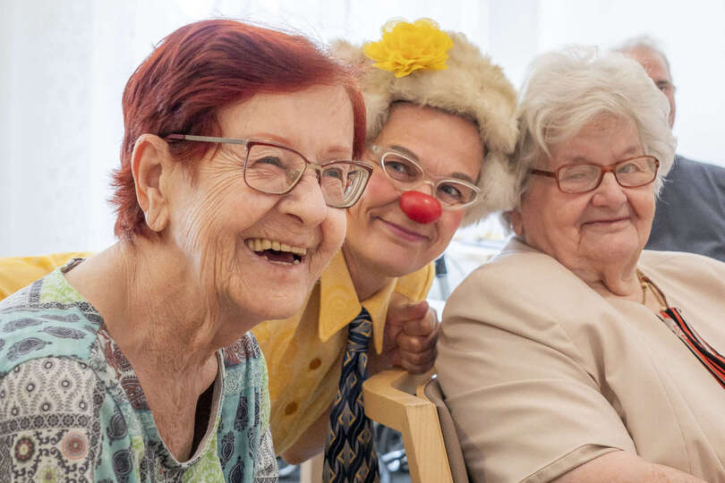 Clownin Zitronella lacht mit zwei Seniorinnen im Pflegeheim.