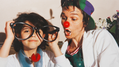 Ein Clown der ROTE NASEN und ein Kind, dass eine übergroße Brille in den Händen hält.