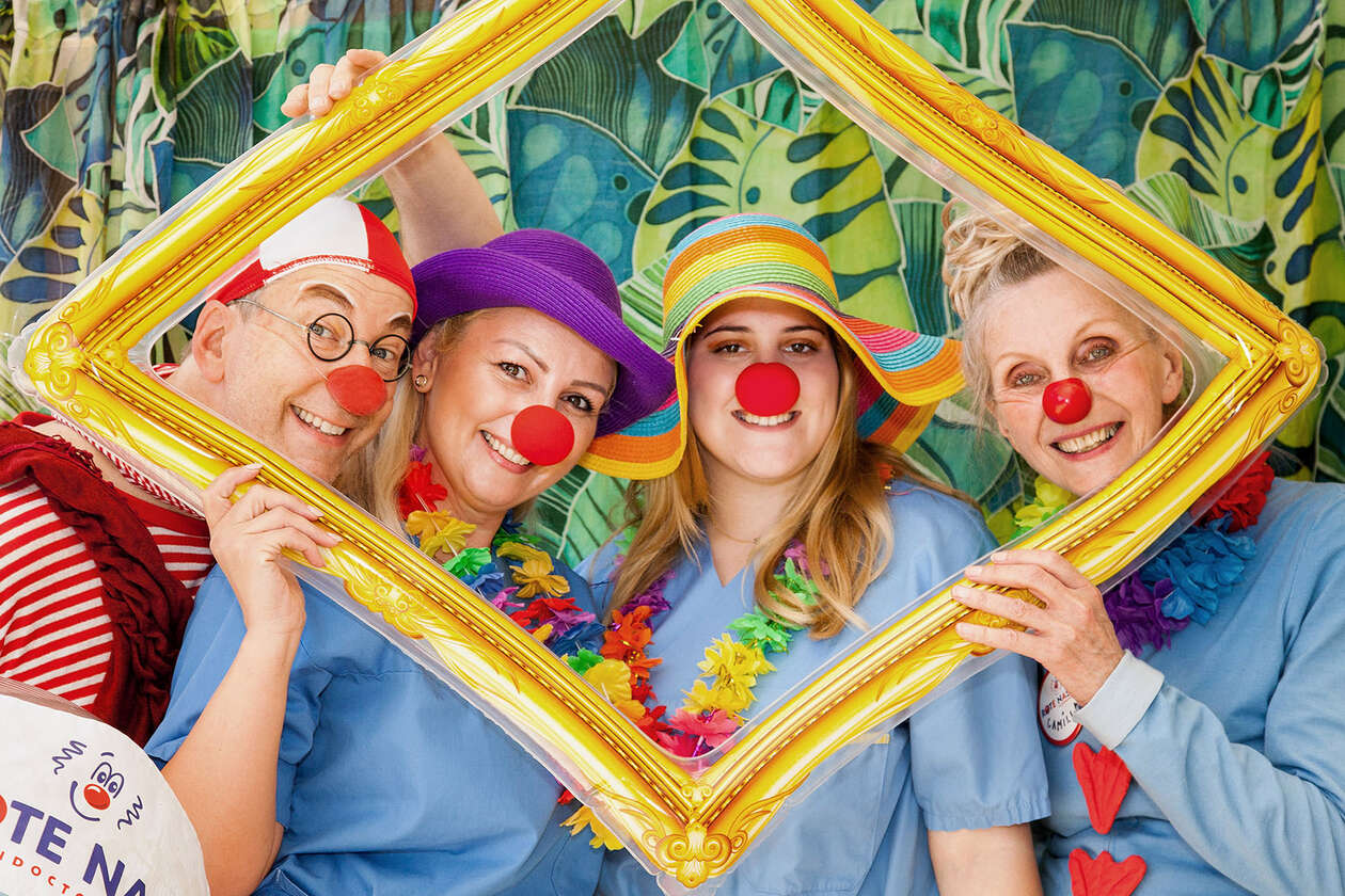 Zwei Clowns und zwei Krankenhausmitarbeiterinnen posieren in sommerlichen Outfits und mit Requisiten für ein Foto