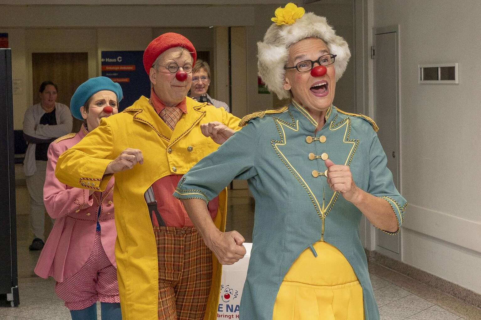 ROTE NASEN Clowns in bunten Kostümen laufen fröhlich lachend durch einen Flur.