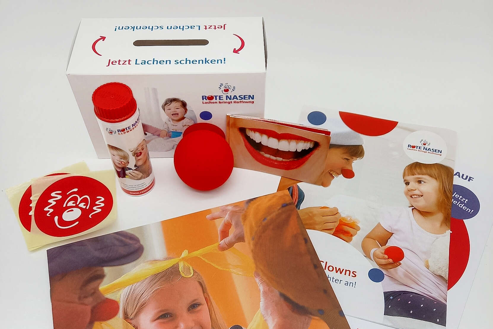 Verschiedene Materialien aus dem ROTE NASEN Spendenaktionspaket wie eine Spendenbox, rote Nase, Infofoler.