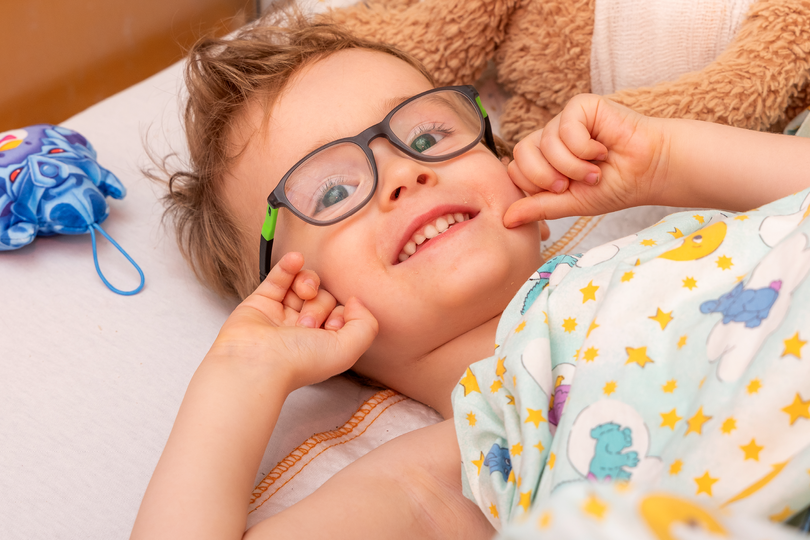 Ein kleiner Junge hält seine beiden Hände an sein Gesicht und lächelt in die Kamera.